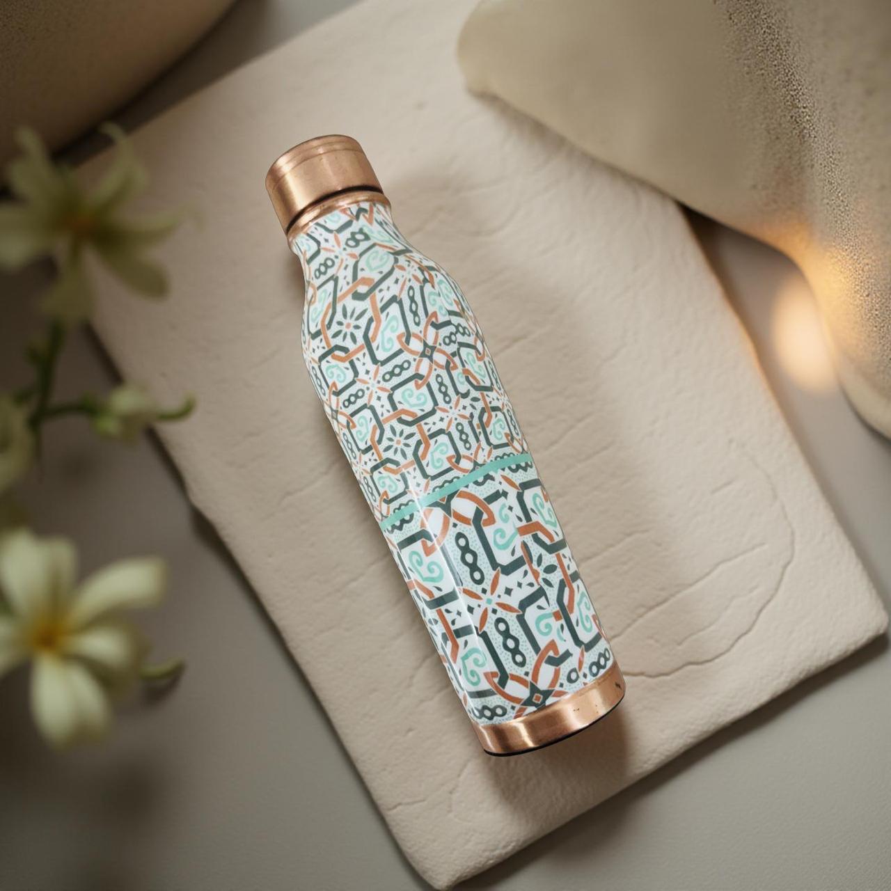 Patterned water bottle with rose gold accents on a textured surface with flowers in the background