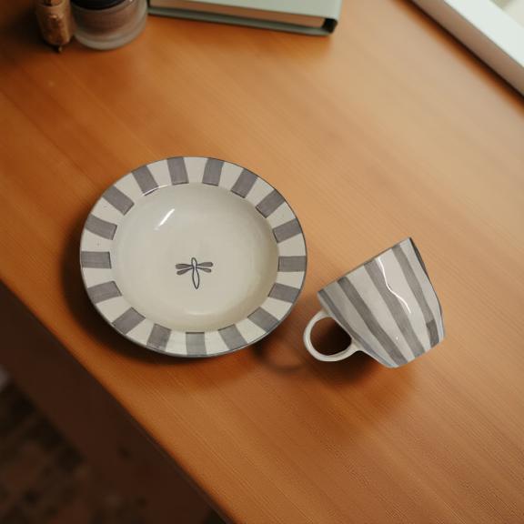 Ceramic cup and saucer with striped design on a wooden surface