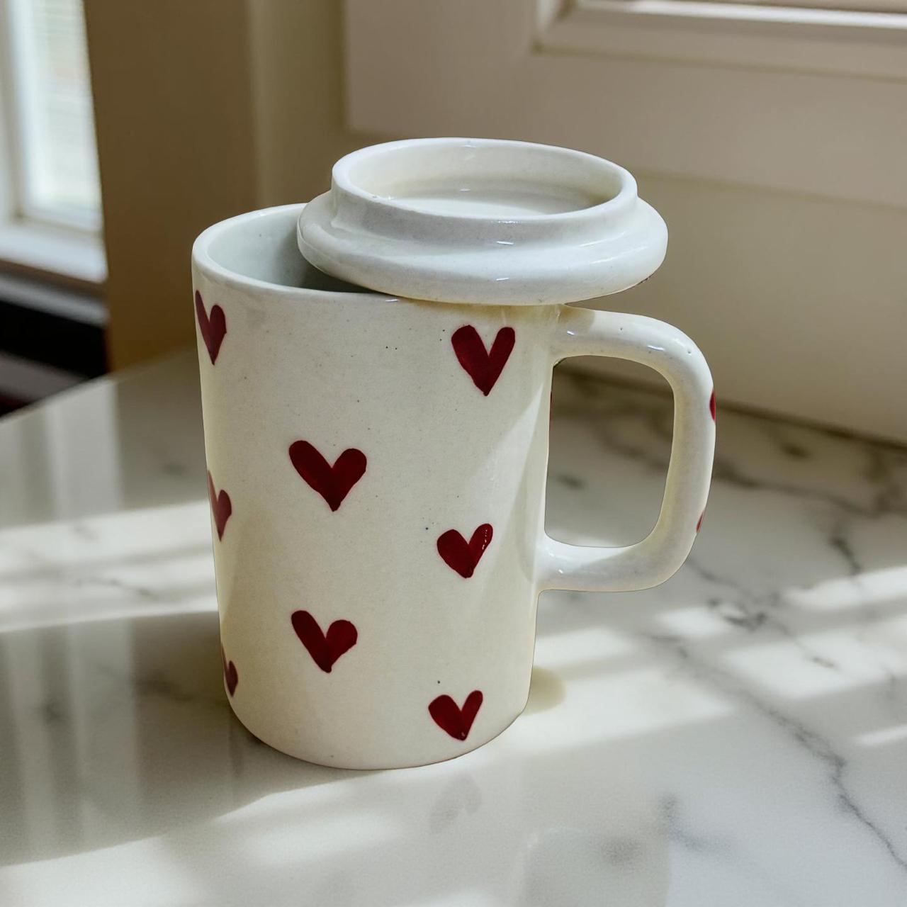 White mug with red heart patterns on a marble surface