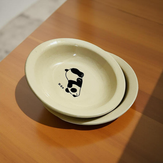 Beige ceramic bowl with sleeping panda print placed on a wooden table