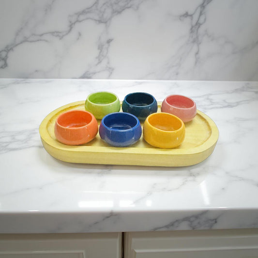 Set of colorful ceramic bowls on a yellow tray against a marble background