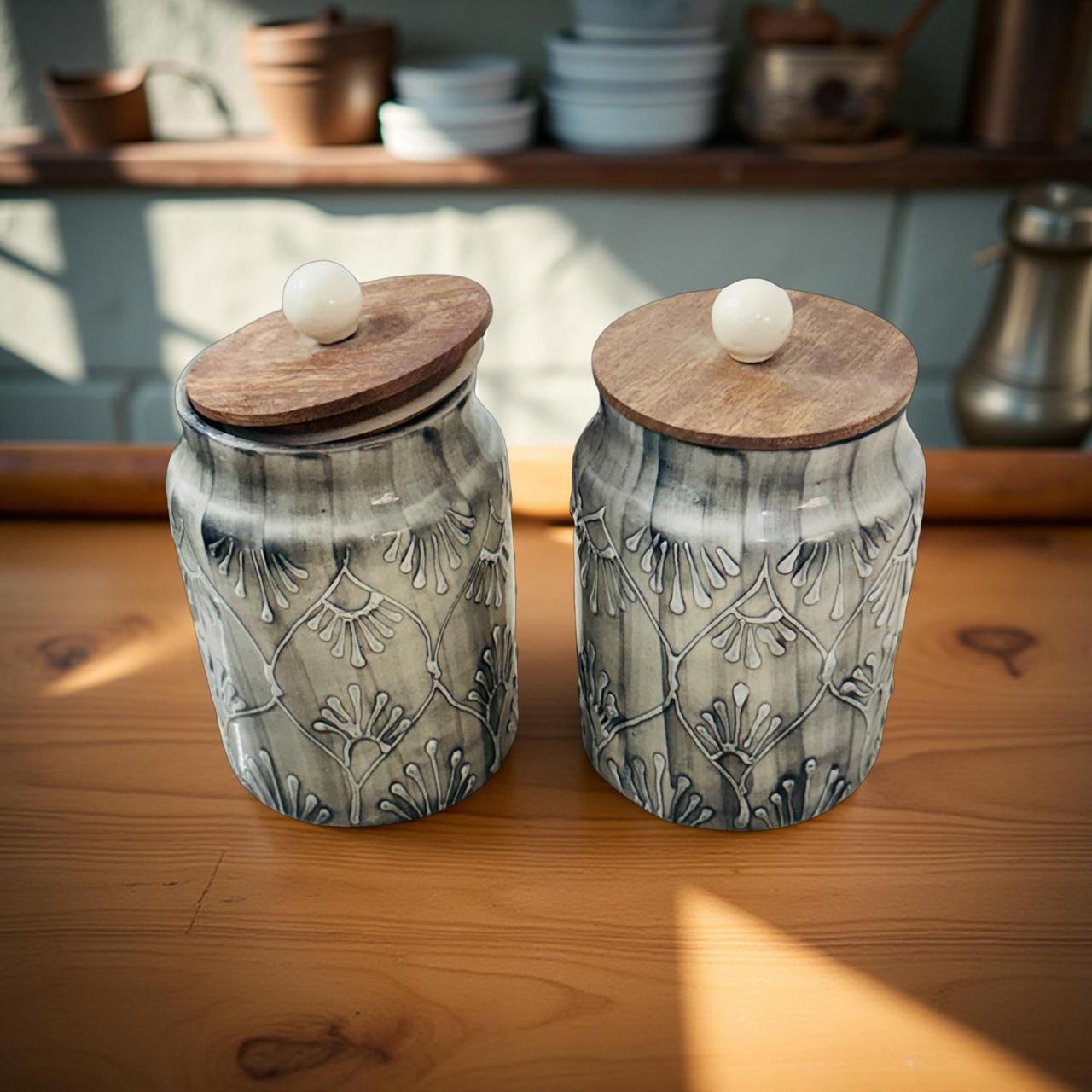 Two ceramic jars with wooden lids on a wooden surface.