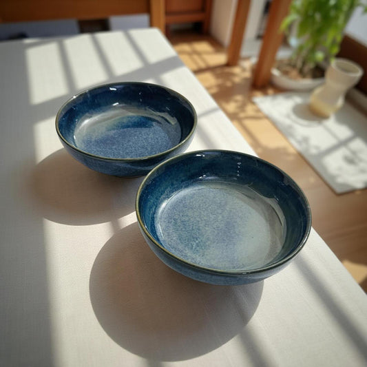 Two blue ceramic bowls on a light surface with a blurred indoor background