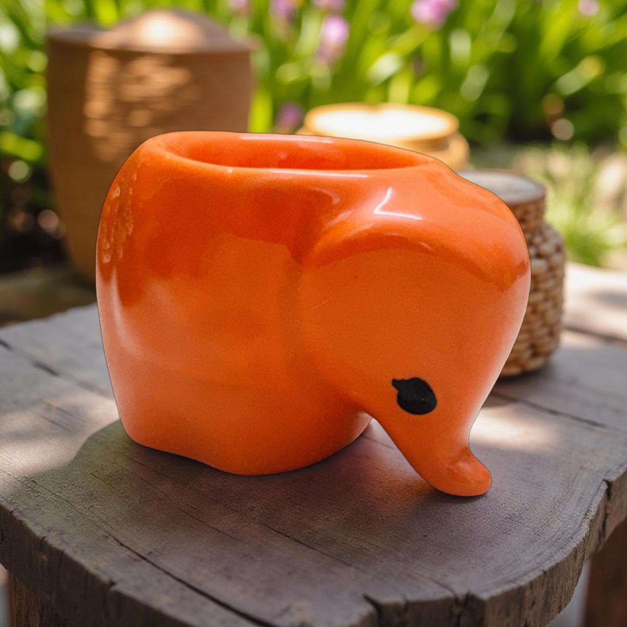 Orange elephant-shaped planter on a wooden surface with a garden background