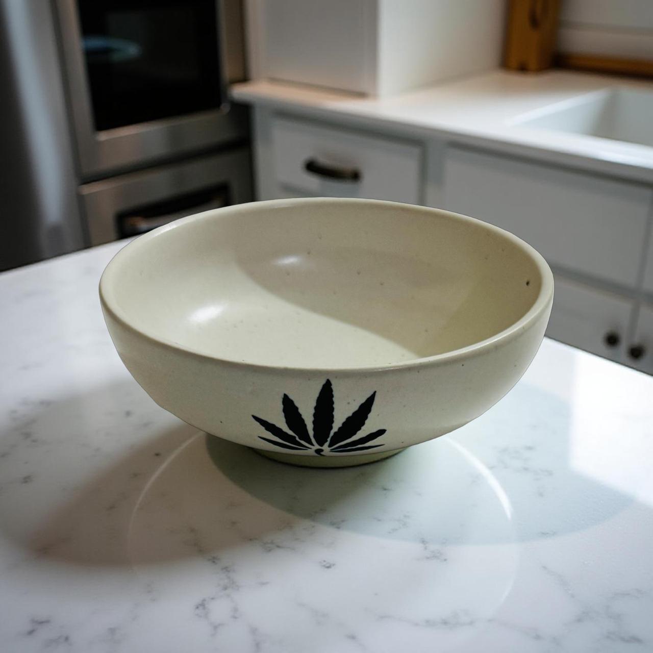 Beige ceramic bowl with a black leaf design on a marble countertop in a kitchen.