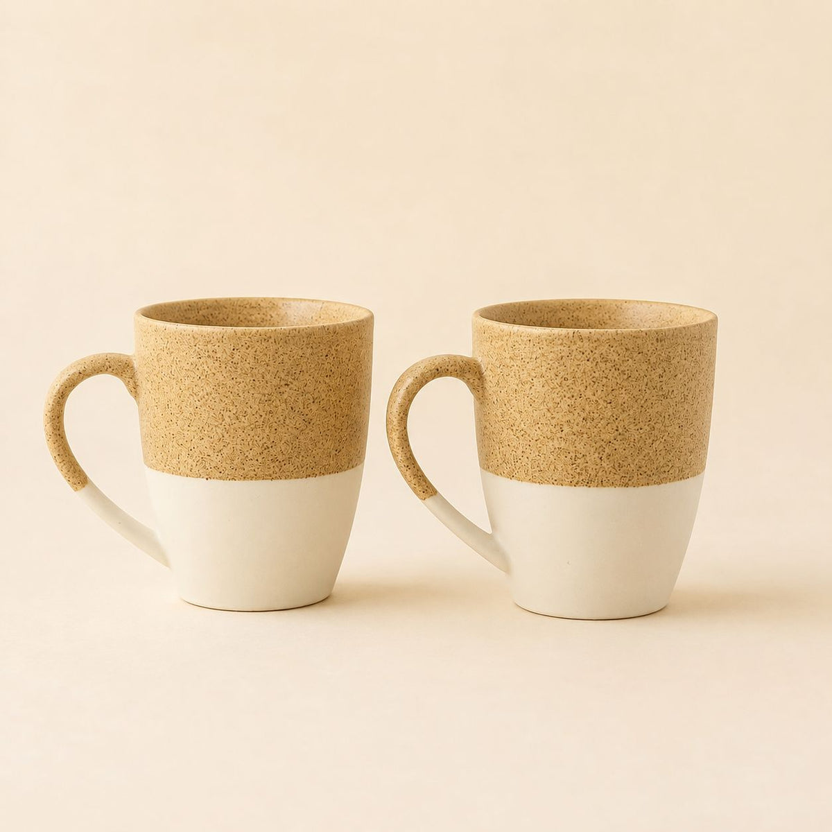 Two ceramic mugs with a two-tone design, featuring a speckled beige upper half and a smooth white lower half, set against a solid beige background.