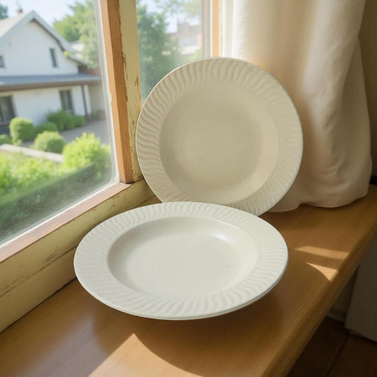 Two beige ceramic plates on a windowsill with a view of a house and trees outside.
