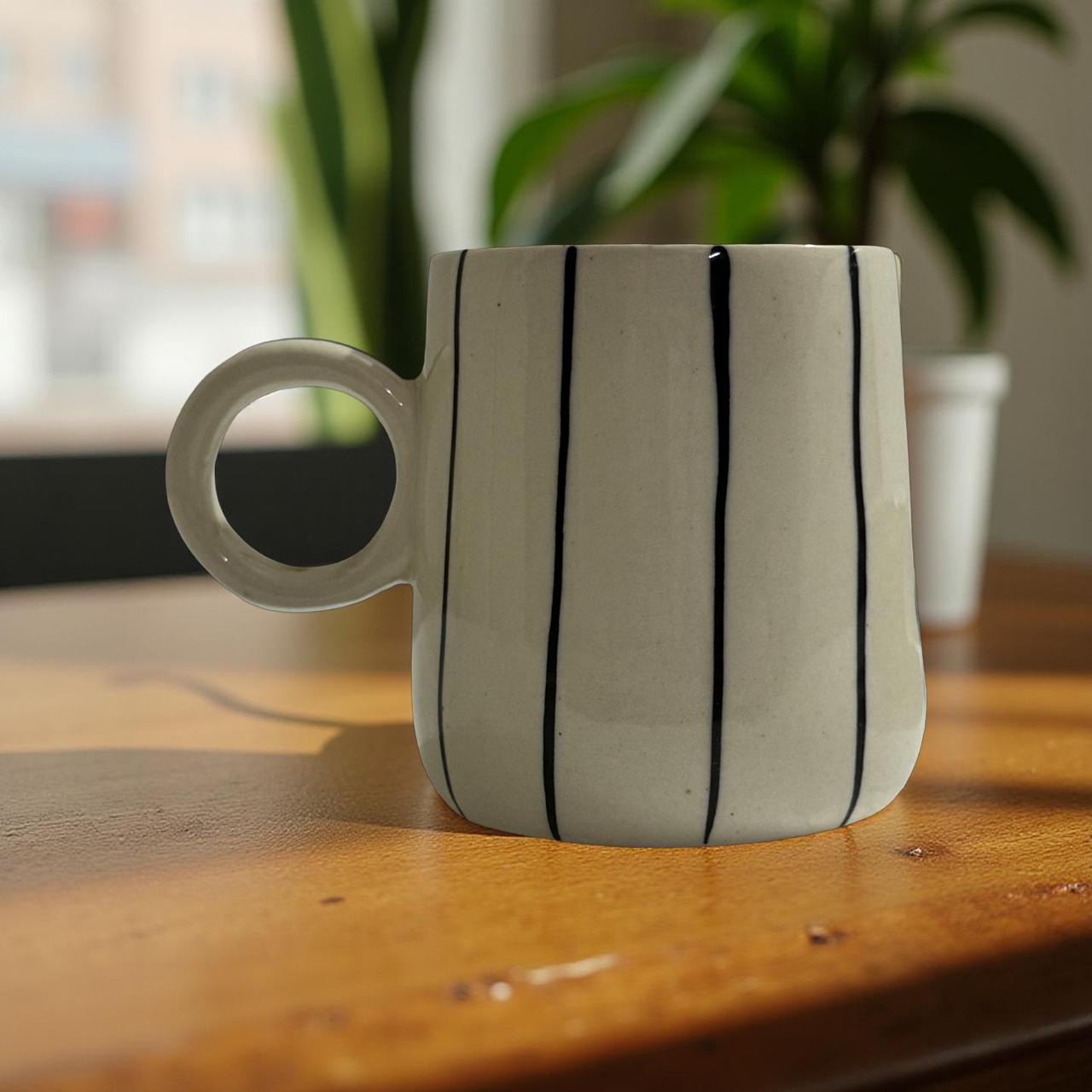 White mug with black stripes on a wooden surface with a blurred plant in the background