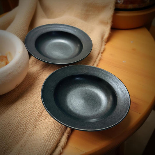 Two black ceramic bowls on a wooden surface with a beige cloth.
