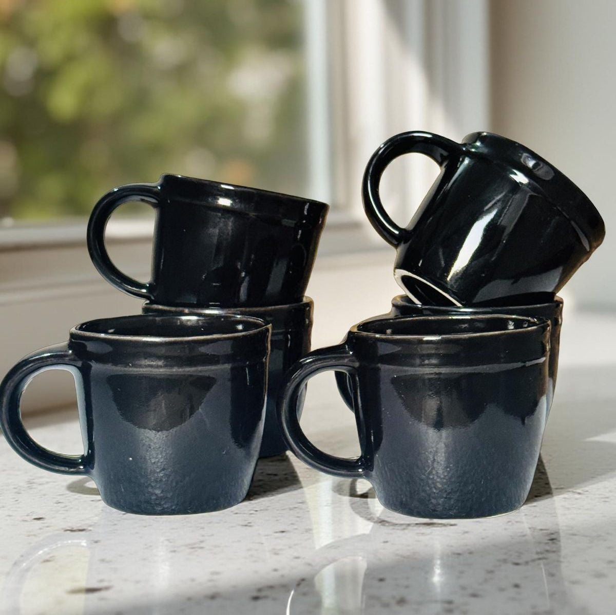 Set of black mugs on a marble surface with a blurred outdoor background