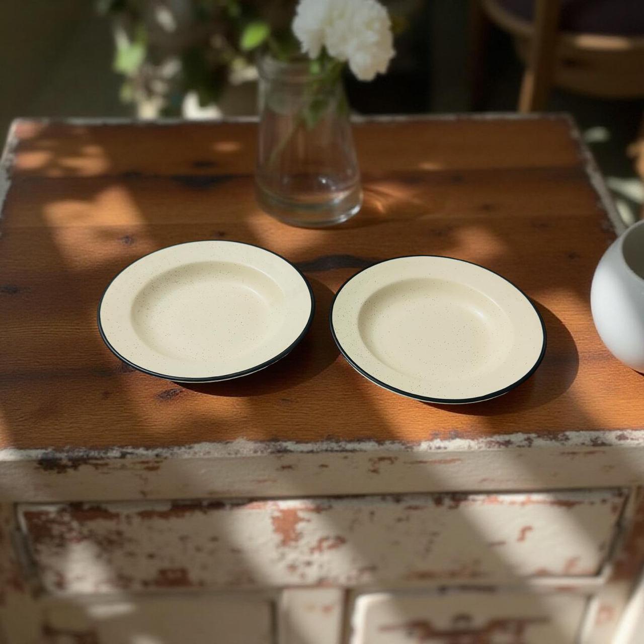 Two ceramic plates on a wooden table with a vase of flowers in the background.