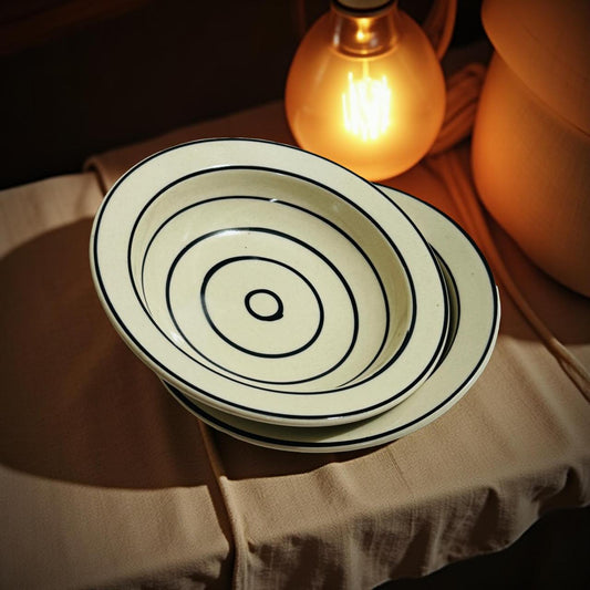 Stack of ceramic bowls with concentric circles on a textured surface with a warm light bulb in the background.
