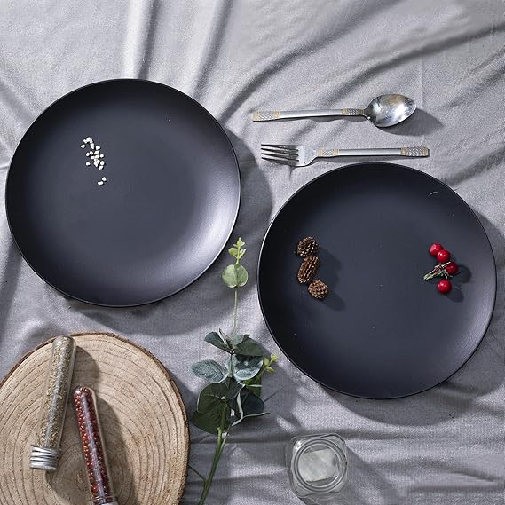 Two black plates with decorative items on a gray surface with cutlery and a woven mat.