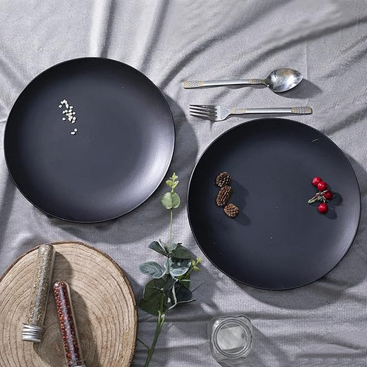 Two black plates with decorative items on a gray surface with cutlery and a woven mat.