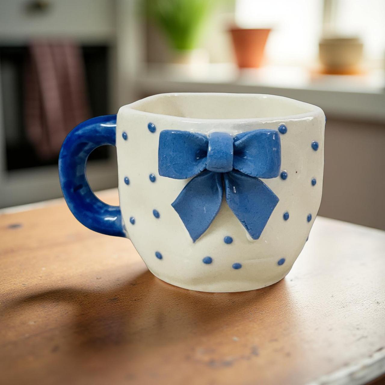 White mug with blue bow and polka dots on a wooden surface