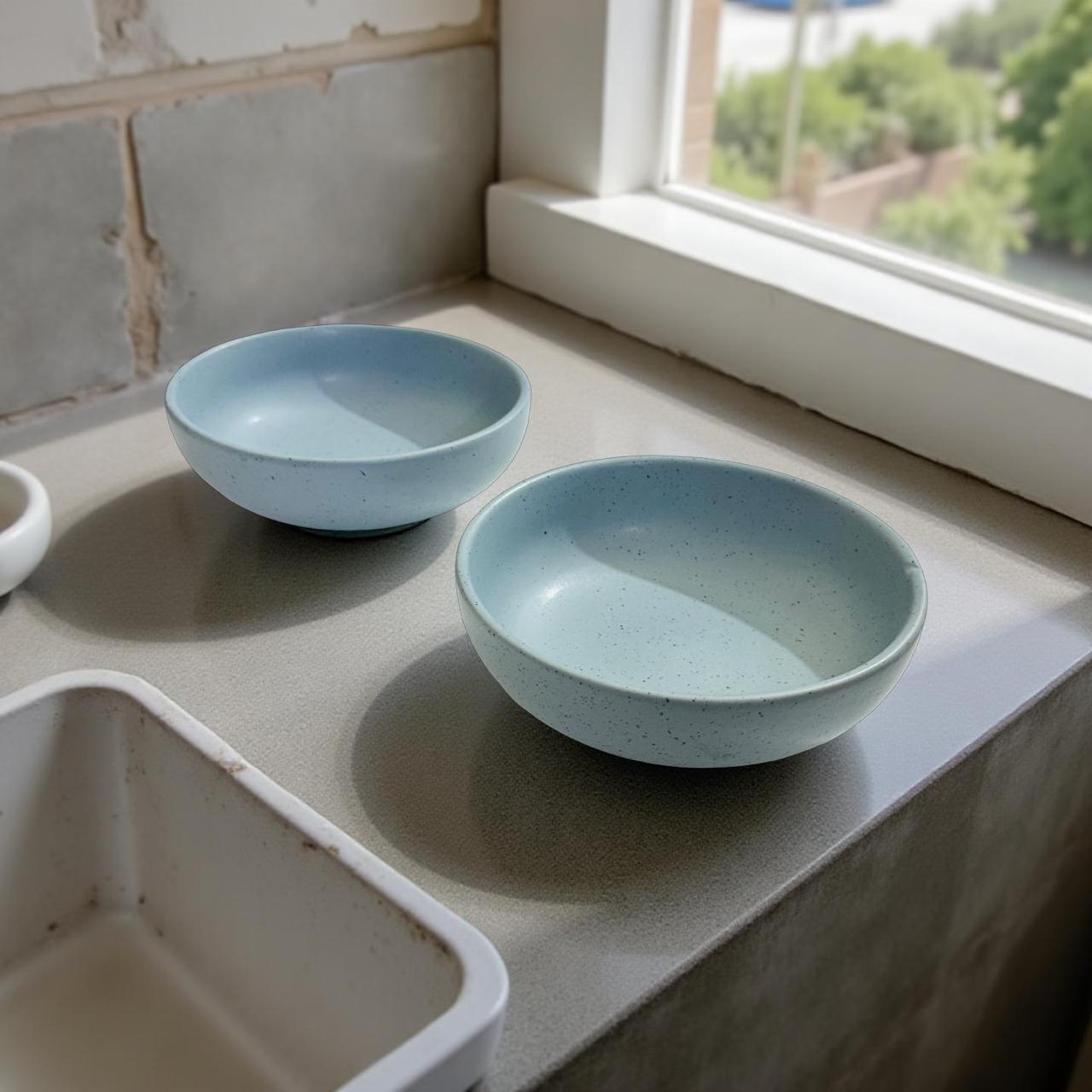 Two light blue ceramic bowls on a kitchen counter near a window.