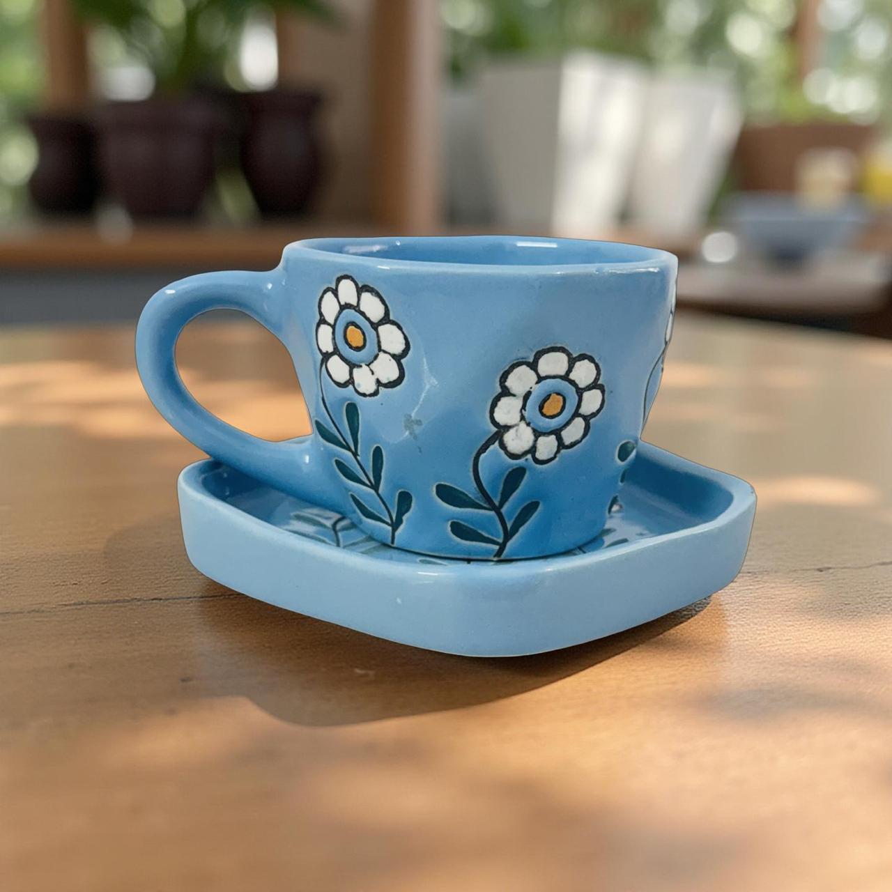 Blue ceramic cup and saucer with floral designs on a wooden surface.
