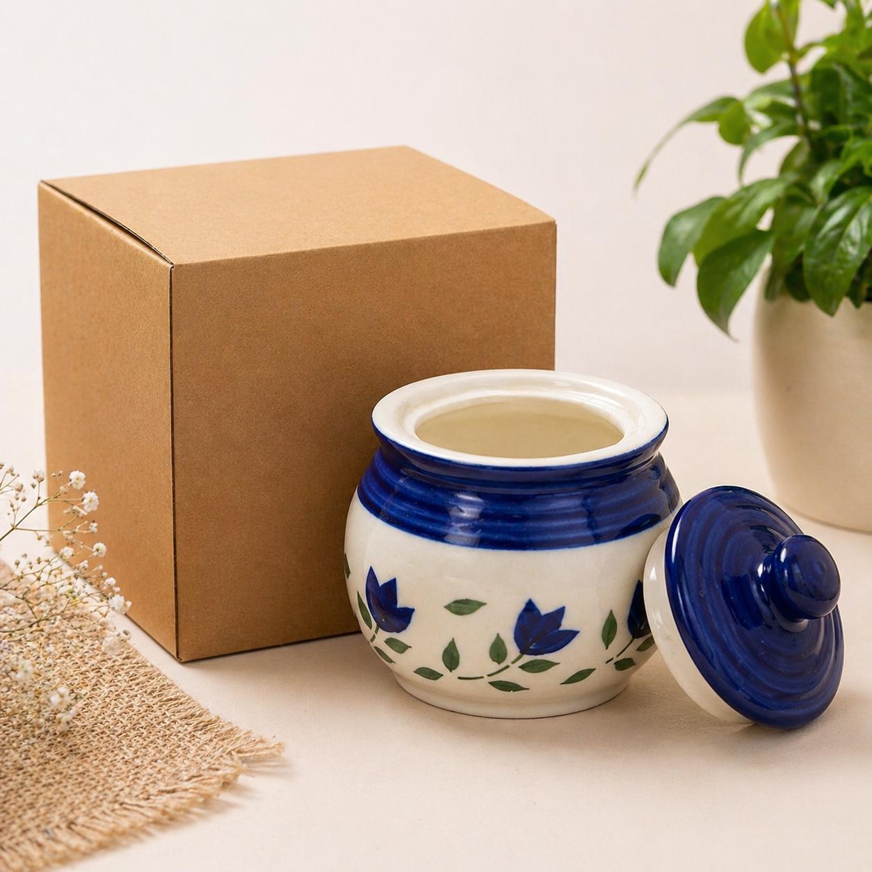 Decorative ceramic jar with blue floral design on a beige surface with a cardboard box and plant in the background.