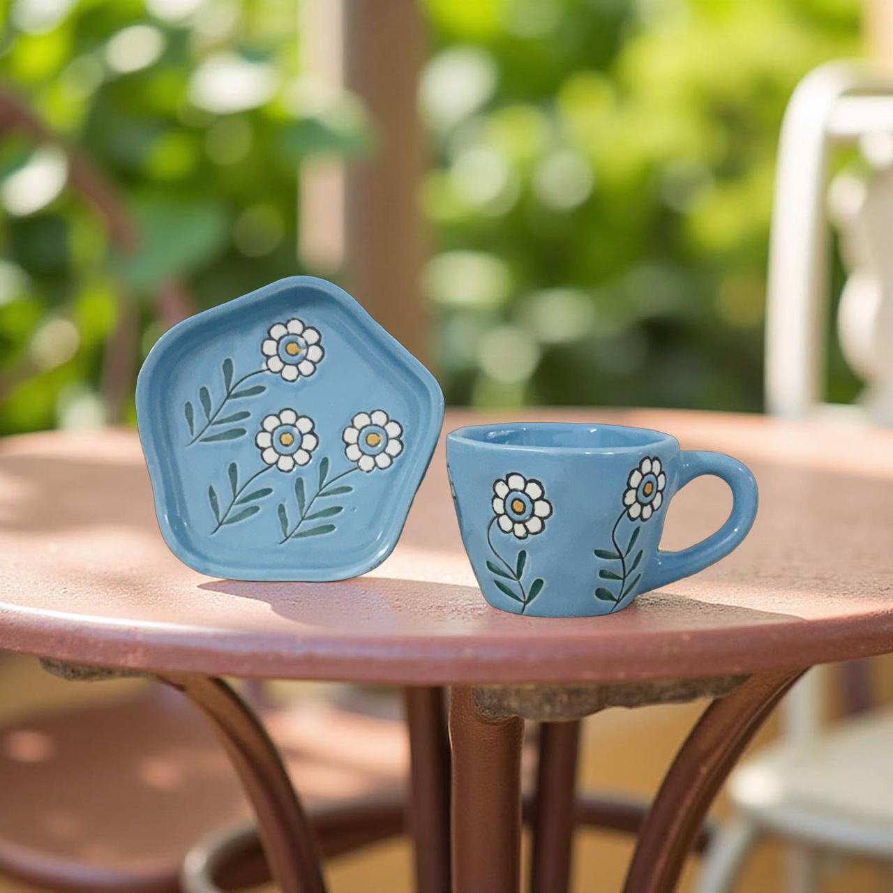 Blue ceramic plate and mug with floral designs on a wooden table outdoors.