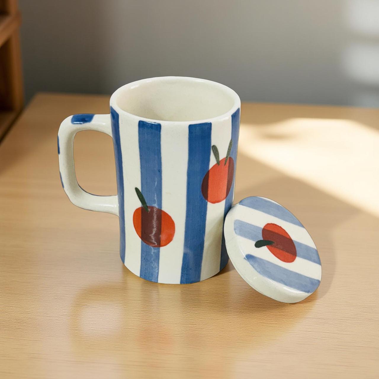 Ceramic mug with blue and white striped design and red apple illustrations on a wooden surface.