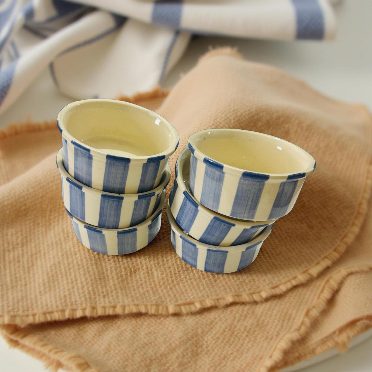 Set of ceramic ramekins with blue and white striped design on a beige cloth.