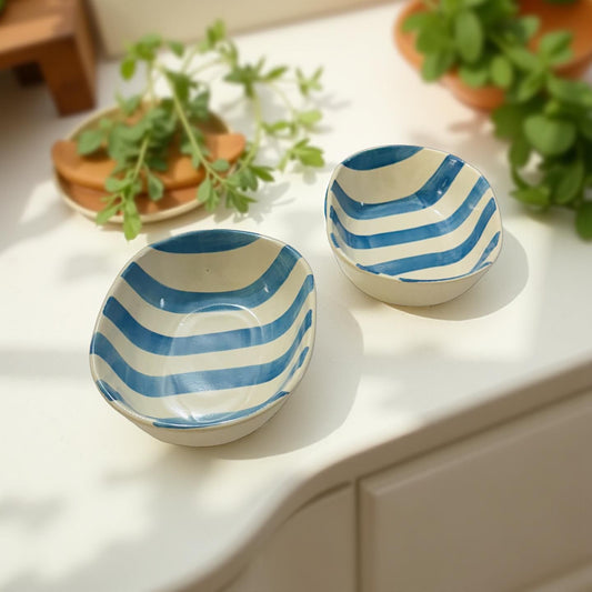 Two ceramic bowls with blue and white striped design on a light surface with plants in the background.