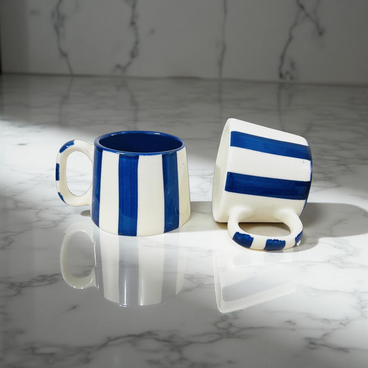 Two blue and white striped ceramic mugs on a marble surface