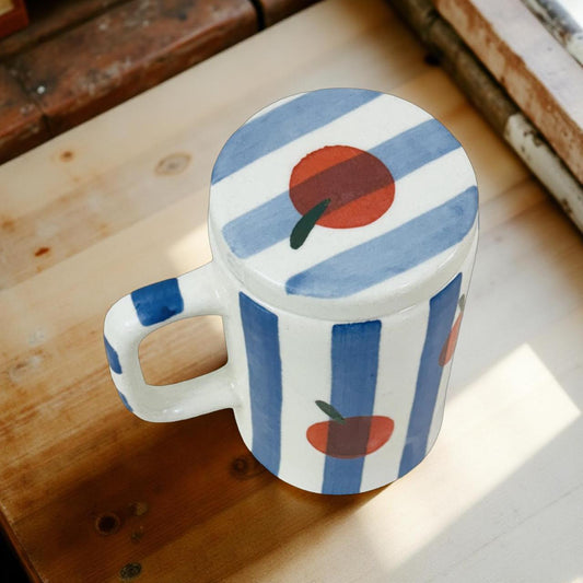 Decorative mug with blue stripes and red circles on a wooden surface