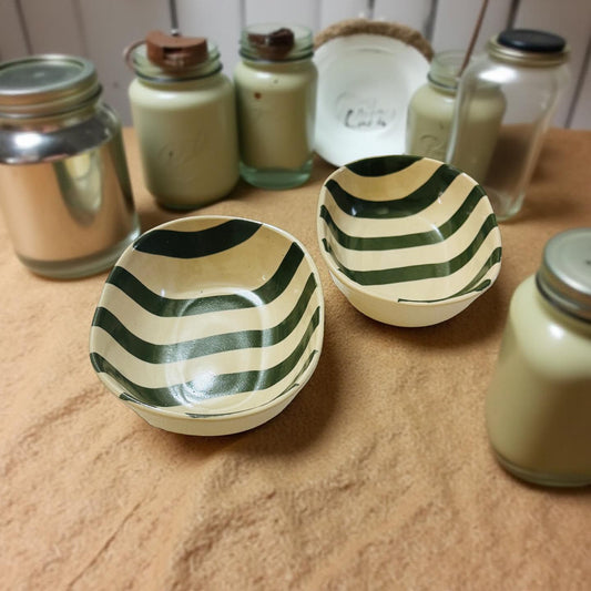 Two ceramic bowls with green and white striped pattern on a wooden surface with jars in the background.