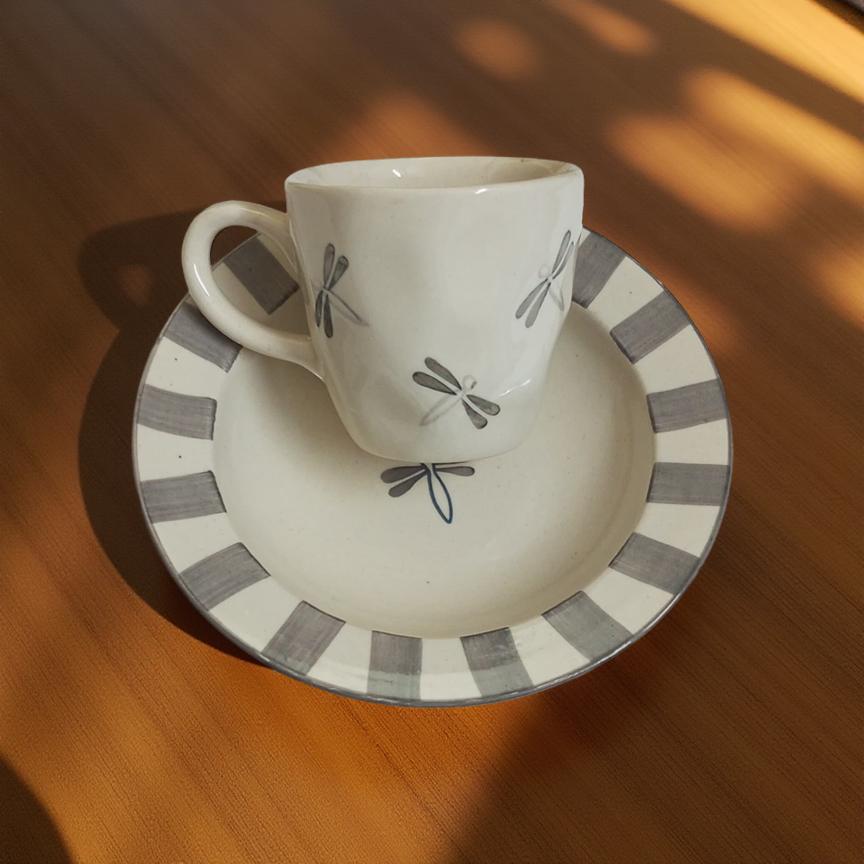 Ceramic cup and saucer with dragonfly design on a wooden surface