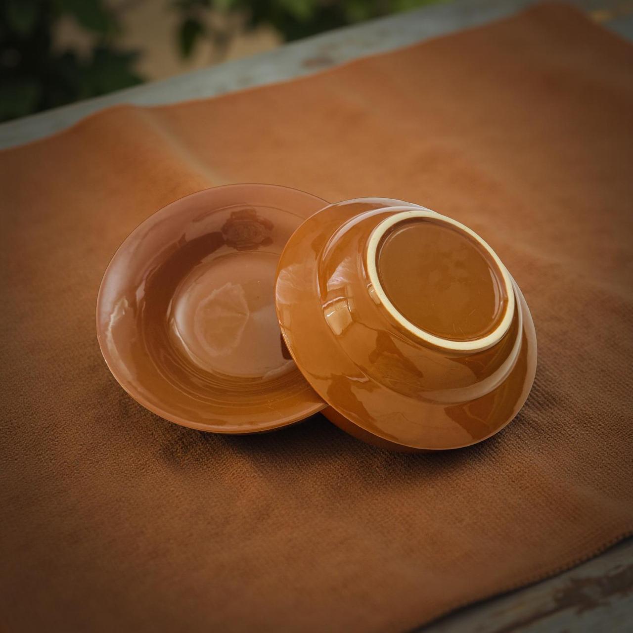 Two orange ceramic bowls on a brown surface with blurred greenery in the background