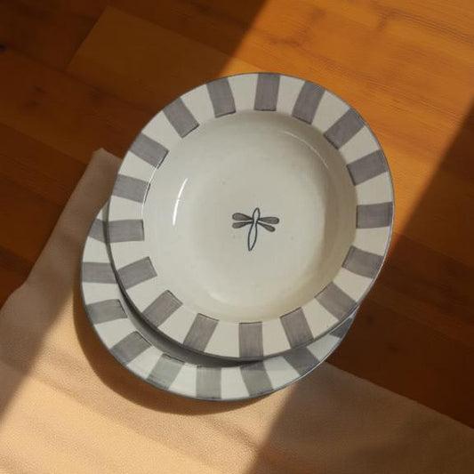 Ceramic plate with gray striped rim and dragonfly design on a wooden surface
