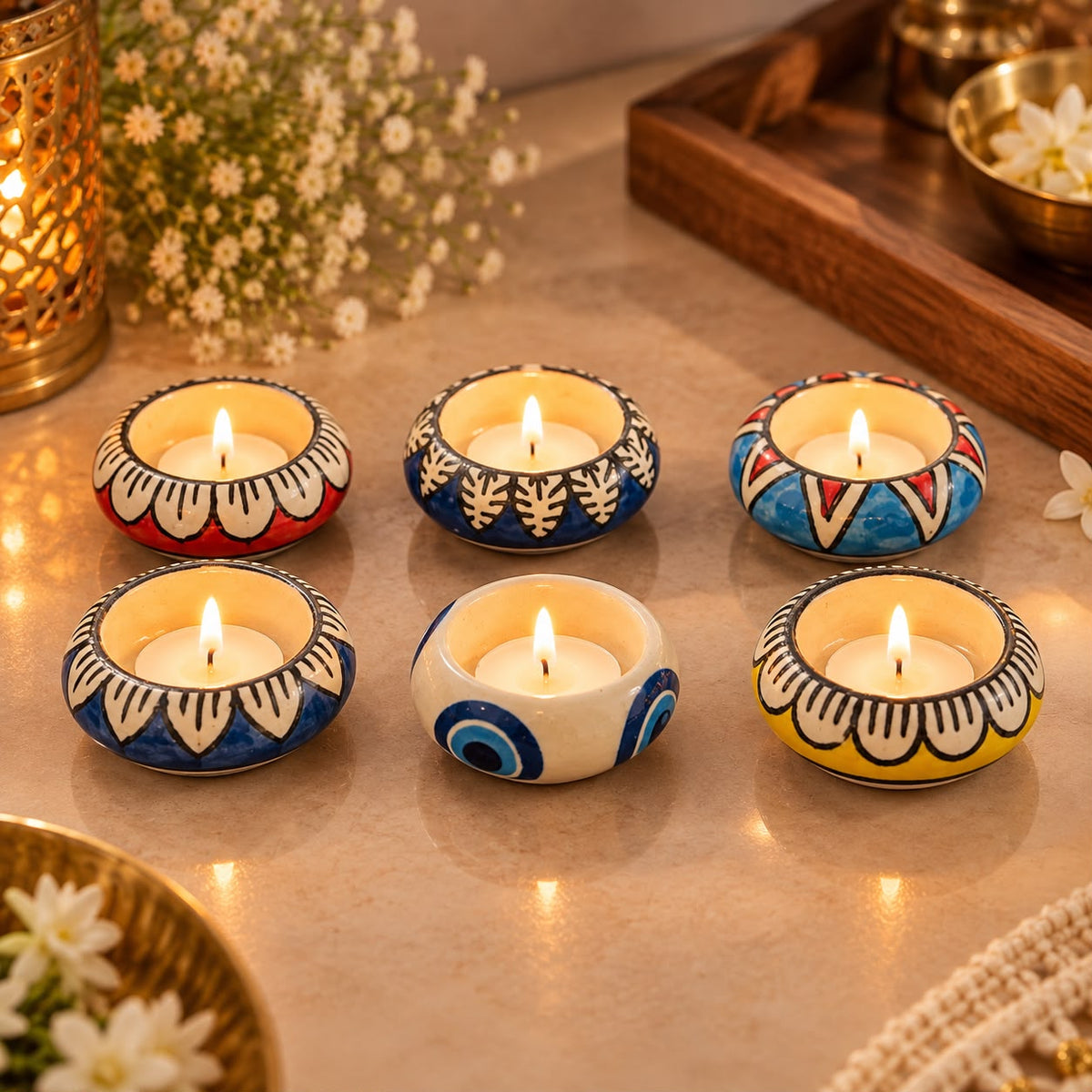 Six small hand-painted ceramic tea light holders arranged on a tabletop, each containing a lit candle. The holders feature colorful traditional patterns in blue, red, yellow, white, and black.