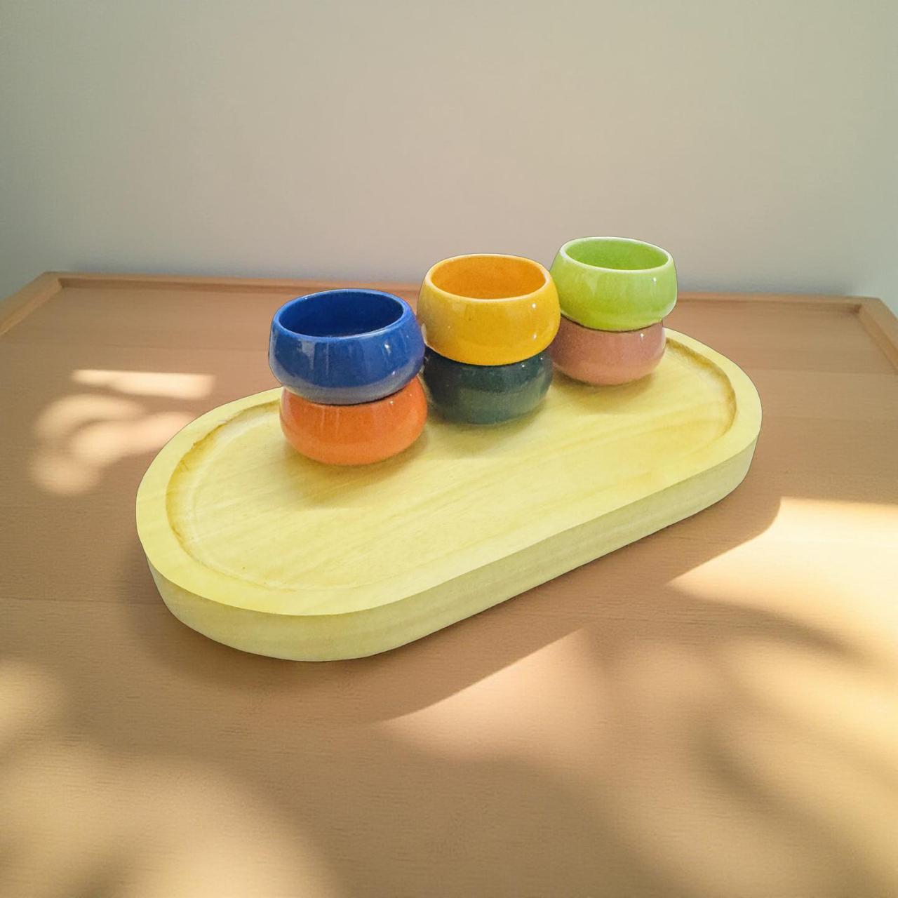 Set of colorful ceramic cups on a wooden tray with a neutral background