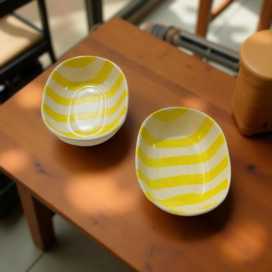 Two yellow and white striped ceramic bowls on a wooden surface.