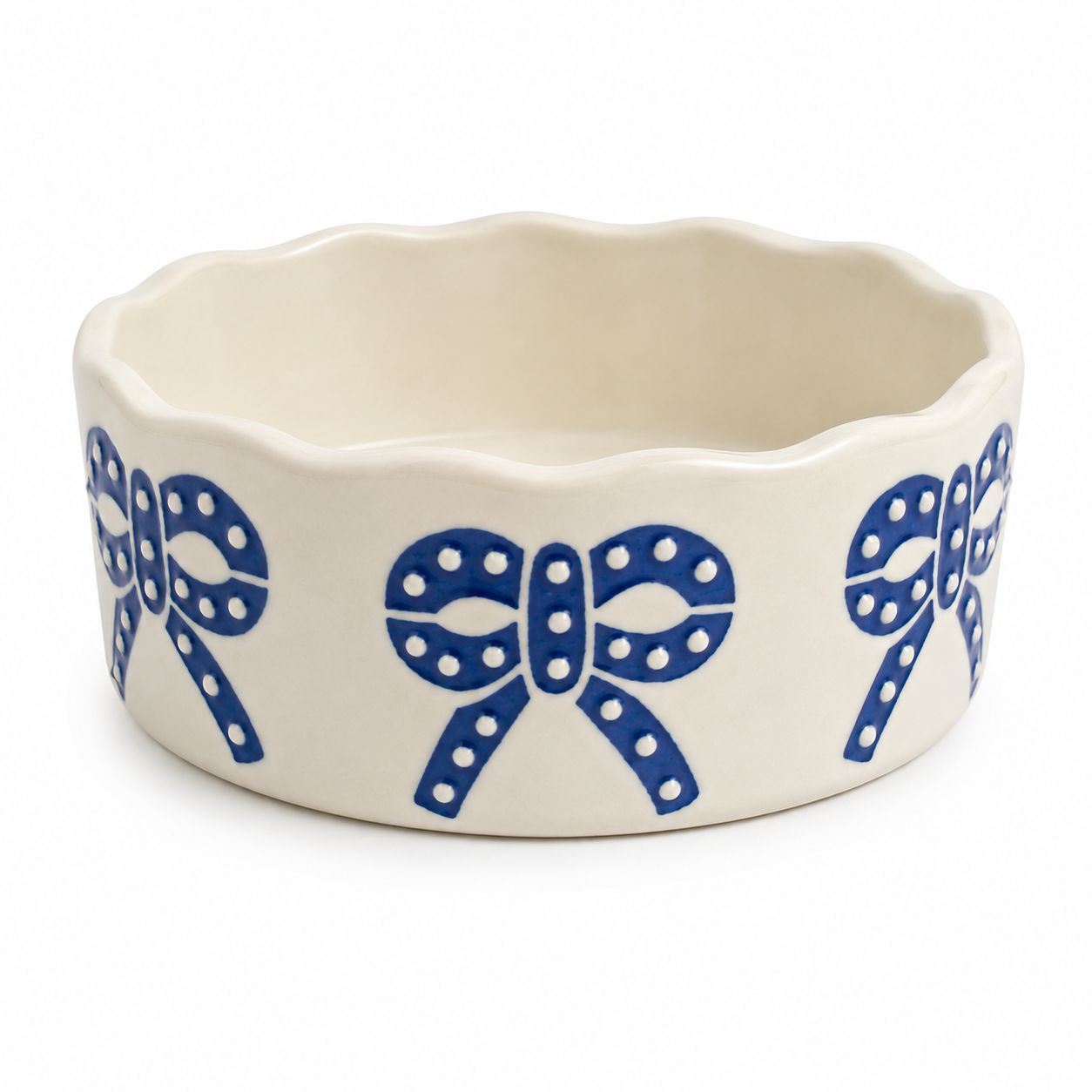 An off-white ceramic bowl with a scalloped rim, decorated with a repeating blue bow pattern featuring white polka dots, shown on a white background.
