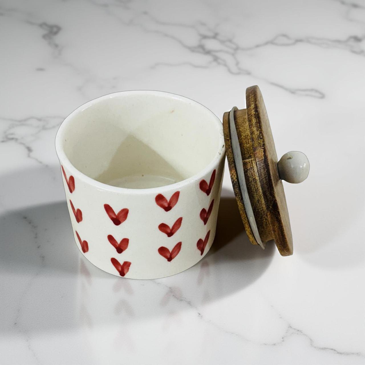 Ceramic container with red heart patterns and a wooden lid on a marble surface