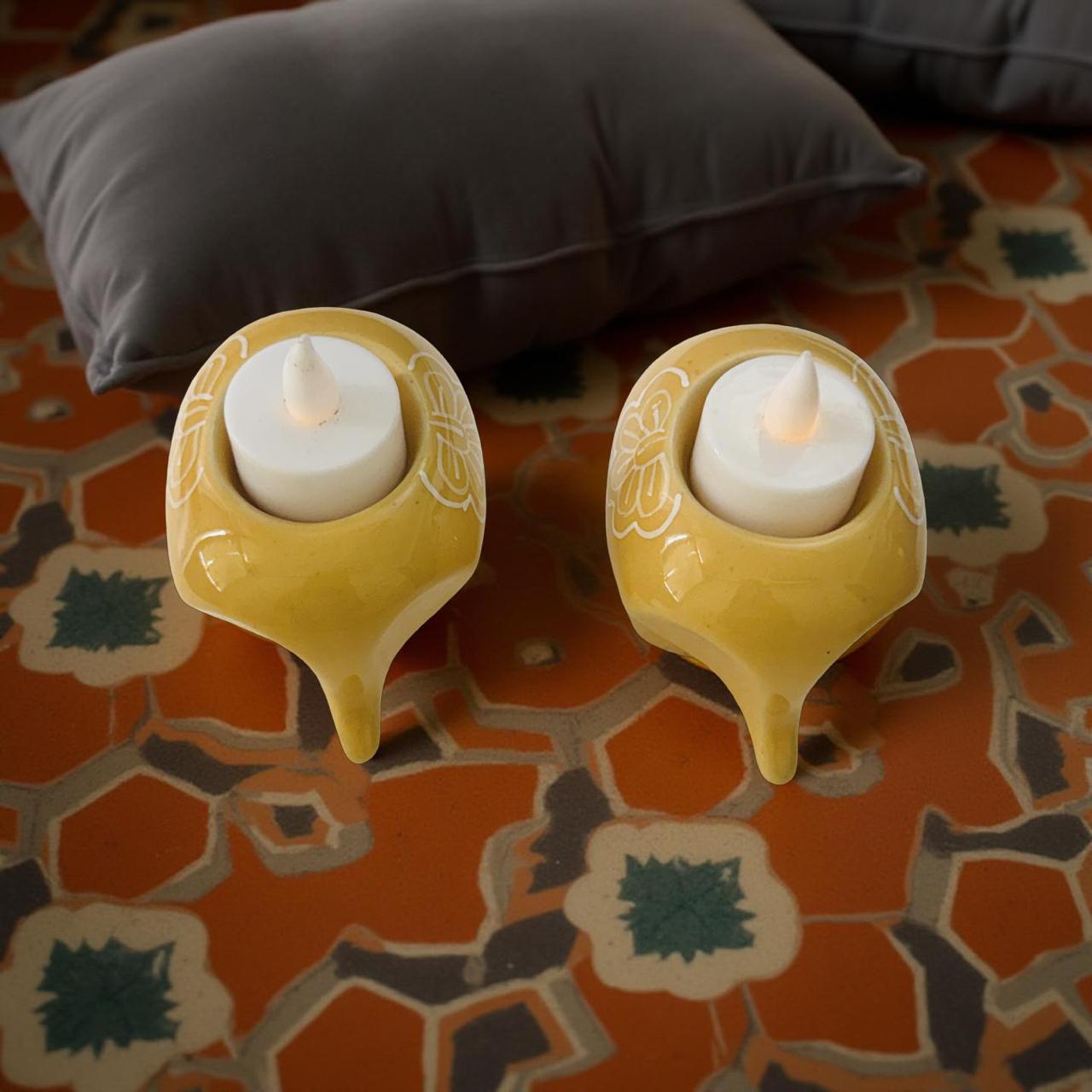 Two yellow ceramic oil lamps with white candles on a patterned fabric background.