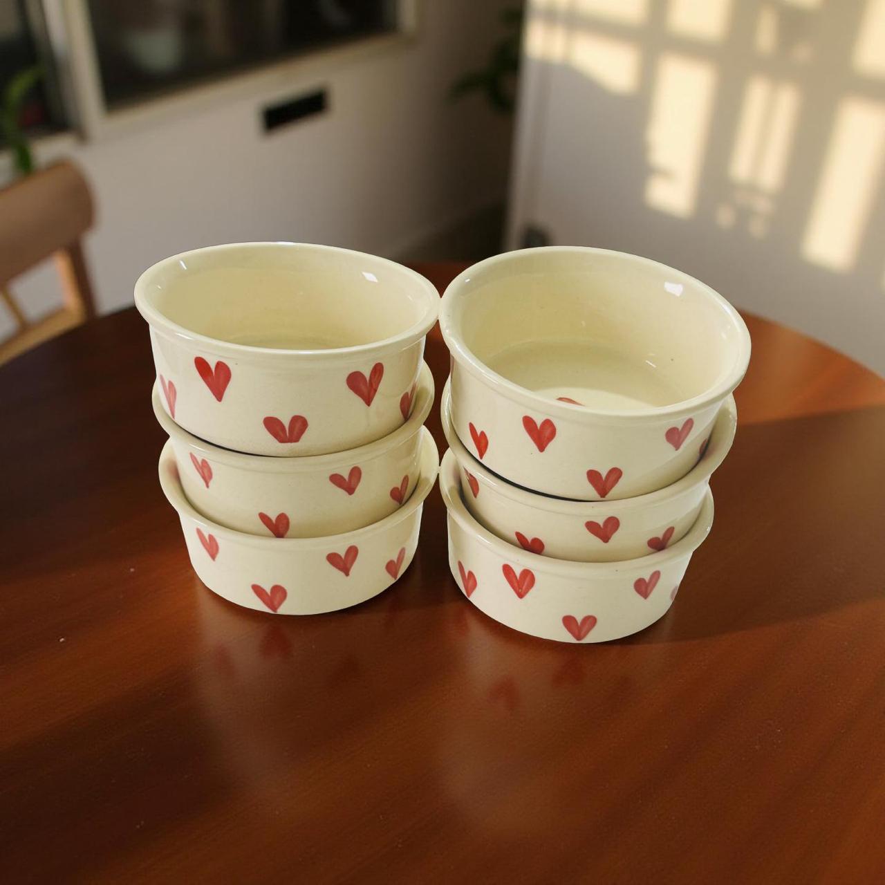 Set of ceramic bowls with red heart patterns on a wooden table