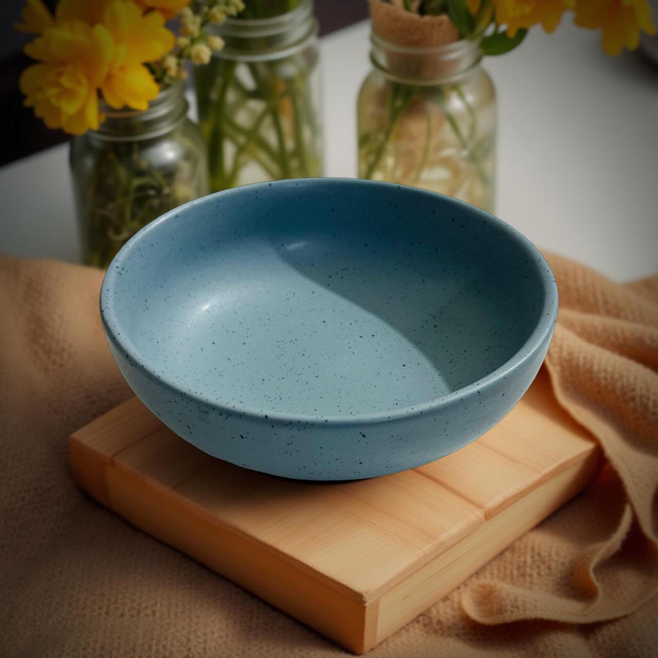 Blue ceramic bowl on a wooden block with jars and flowers in the background