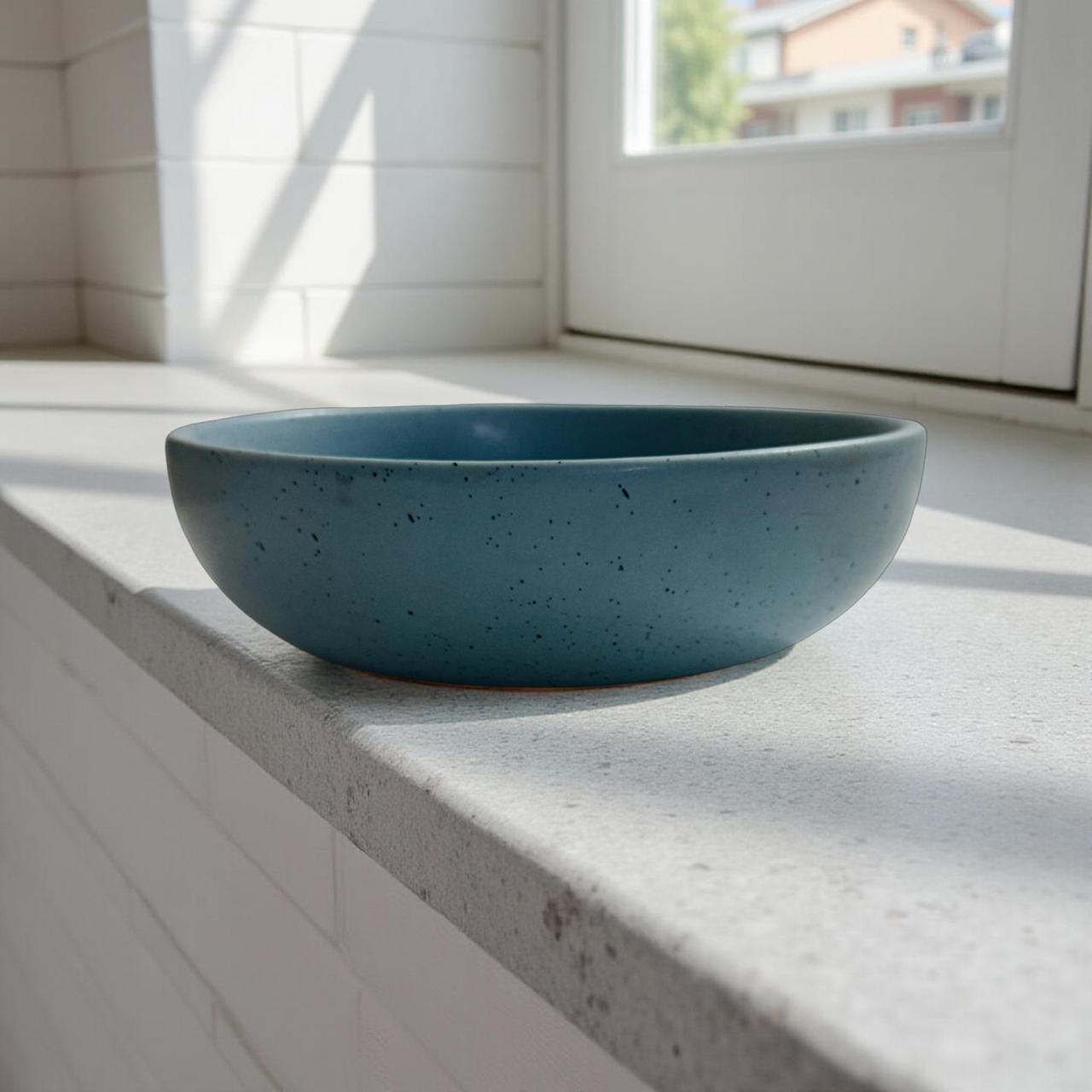 Blue ceramic bowl on a light-colored surface with a window in the background