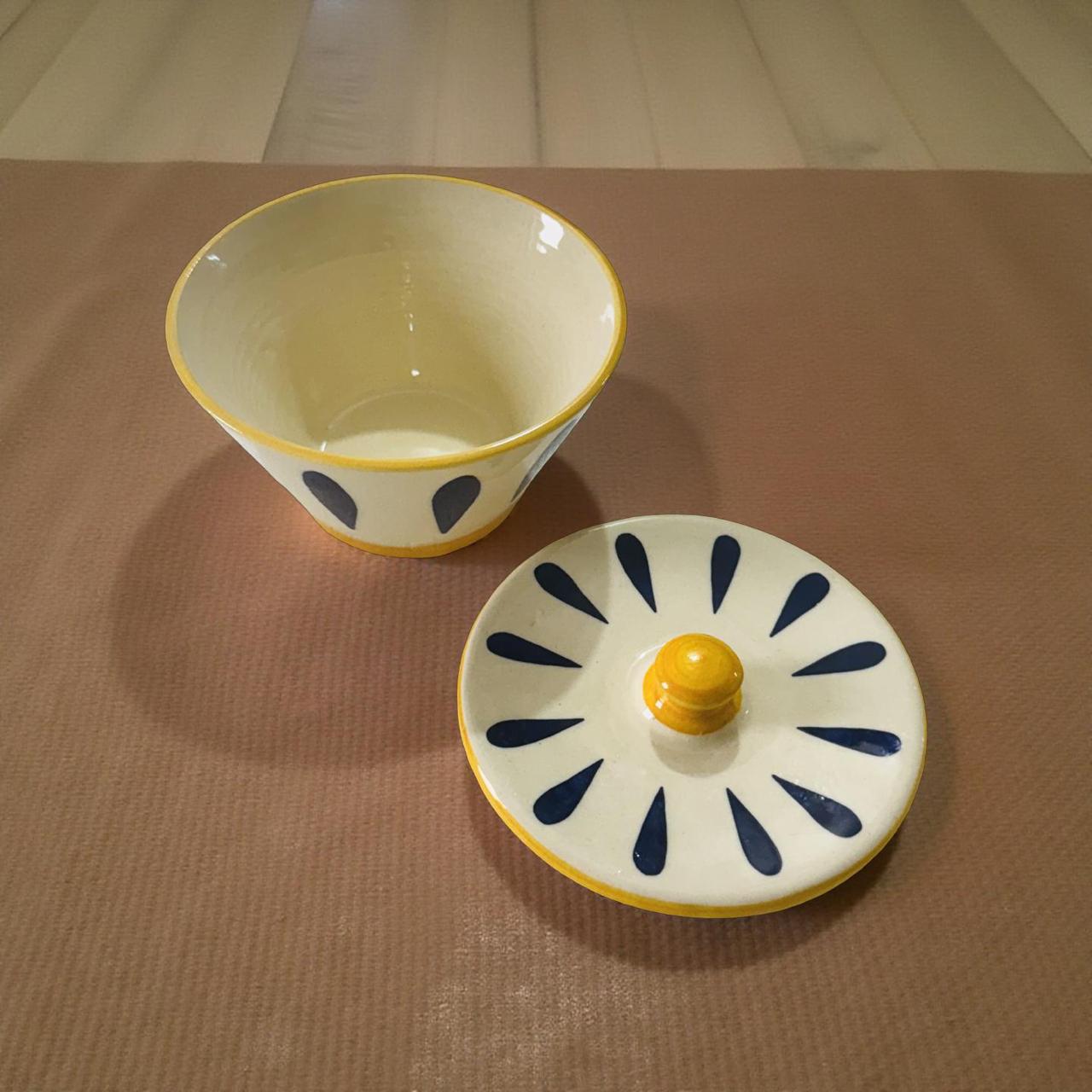 Ceramic bowl with yellow rim and lid featuring blue patterns on a brown surface
