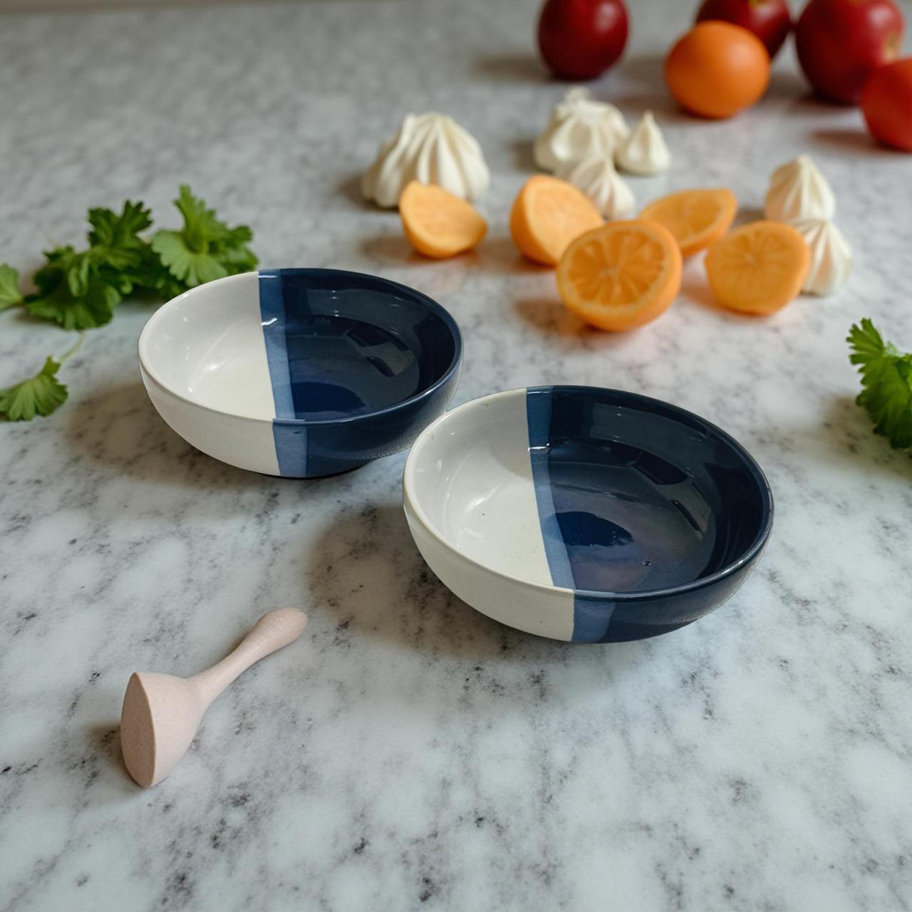 Two blue and white ceramic bowls on a marble surface with fruits and herbs.