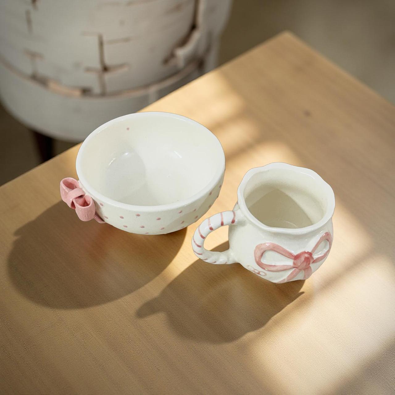 Ceramic cup and bowl set with pink accents on a wooden surface