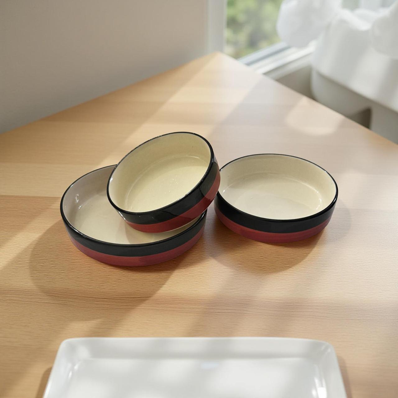 Set of ceramic bowls with red and black rim on a wooden table