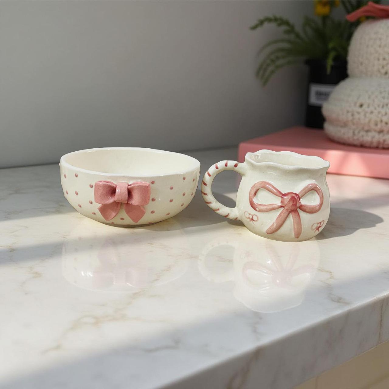 Ceramic mug and bowl set with pink bows on a marble surface