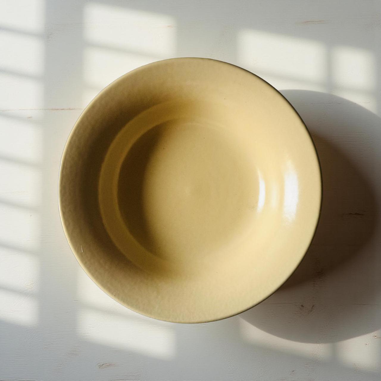 Beige ceramic bowl on a white surface with shadows from natural light