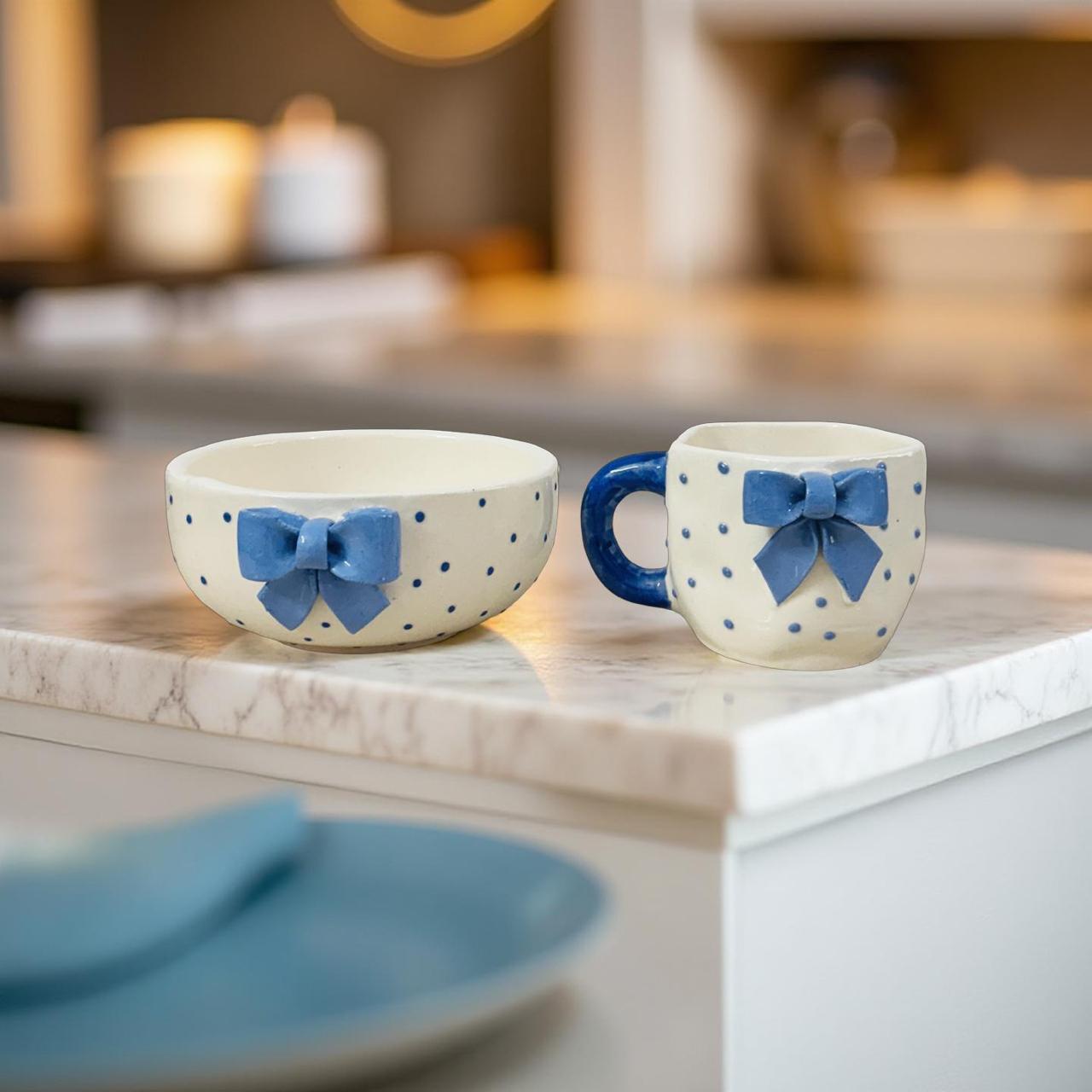 Two ceramic cups with blue bow designs on a kitchen counter.