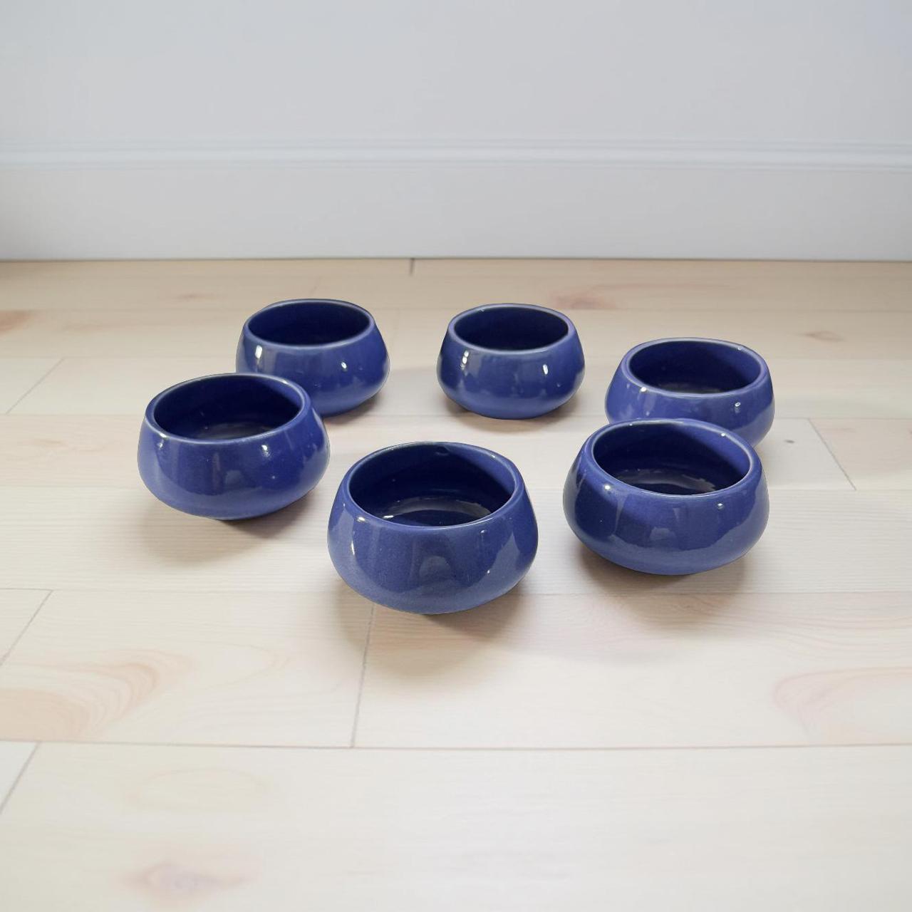 Set of six blue ceramic bowls on a light wooden floor.