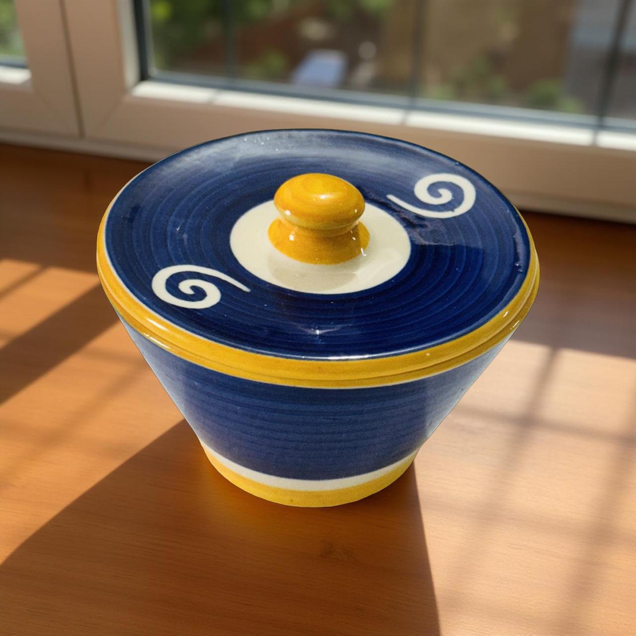 Ceramic container with blue lid featuring a yellow knob on a wooden surface.